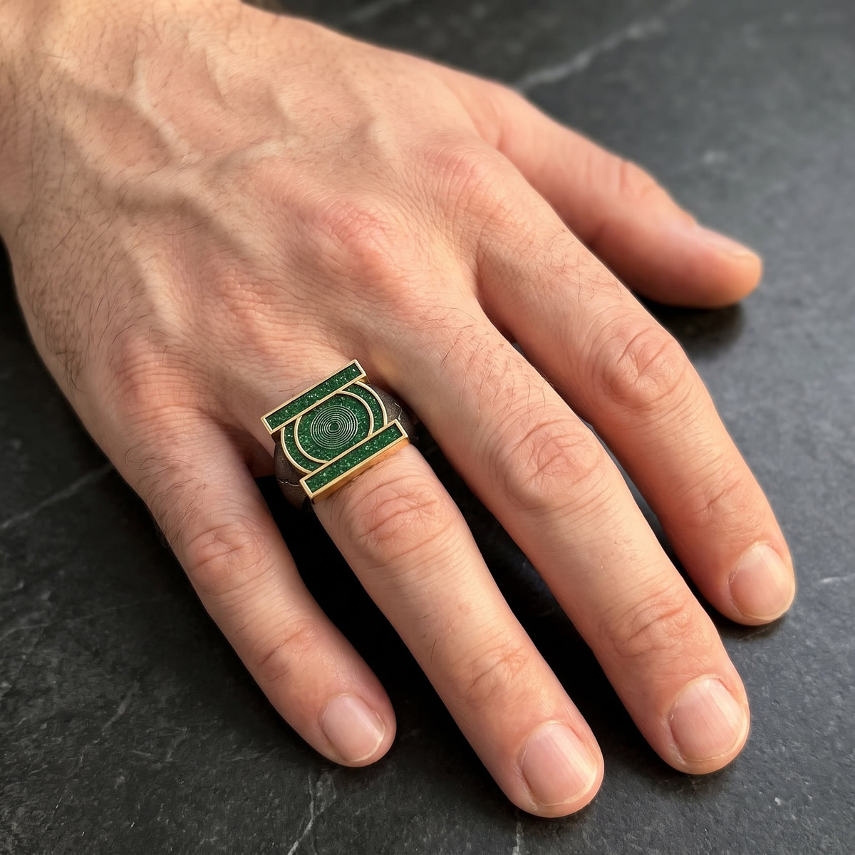 Green emblem copper open ring worn on a male hand with light skin